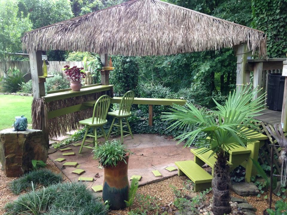 Thatched tiki hut bar and seating area set into a lush backyard garden with palms and stepping stones