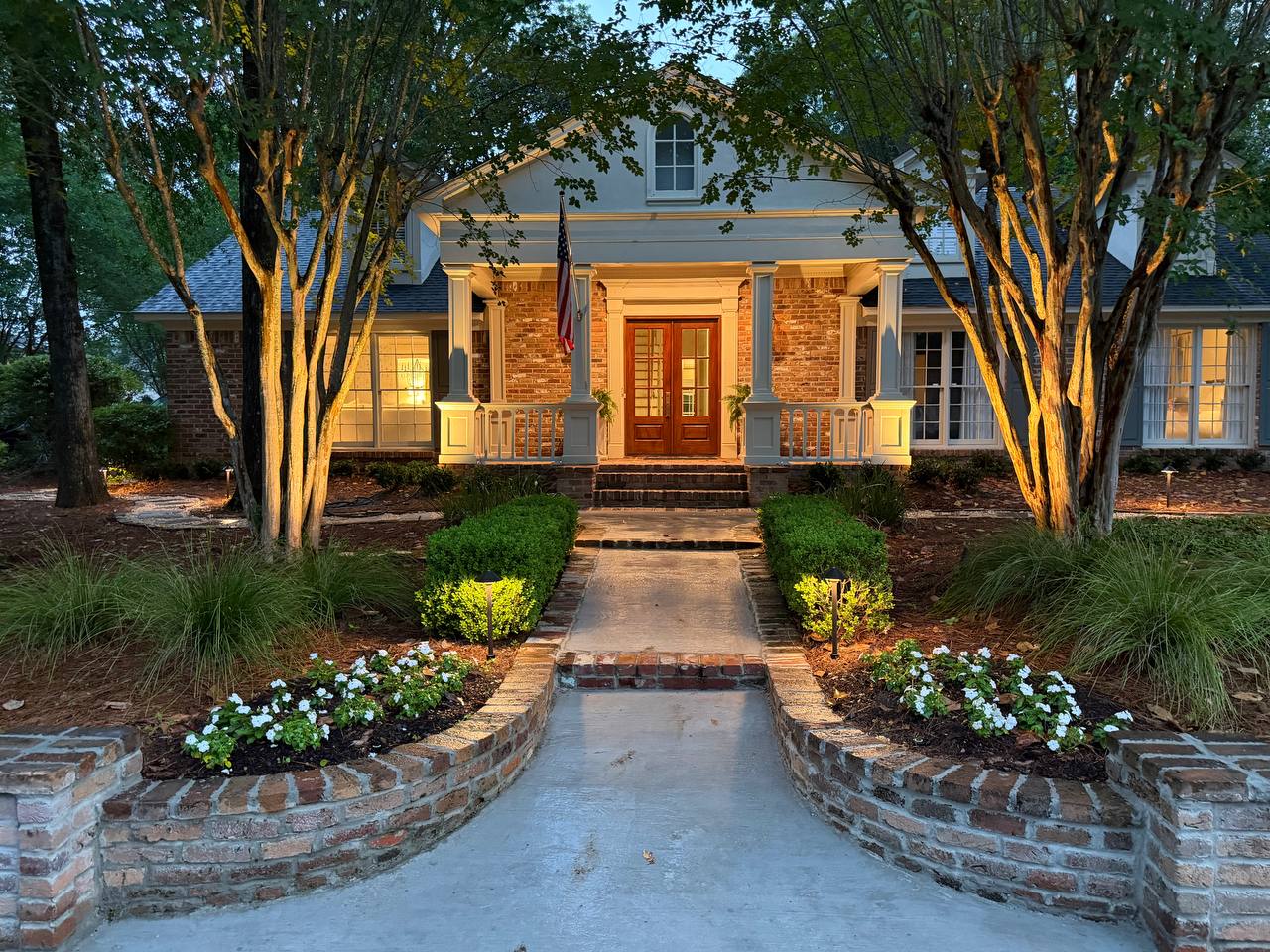 Front walk and entry porch framed by warm path lighting, brick walls, and illuminated crepe myrtles