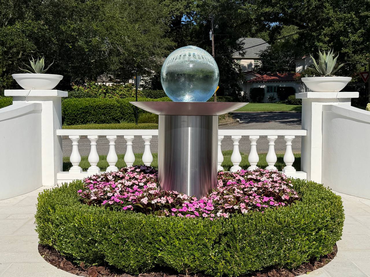 Circular boxwood bed with pink flowers and a sculptural fountain centerpiece